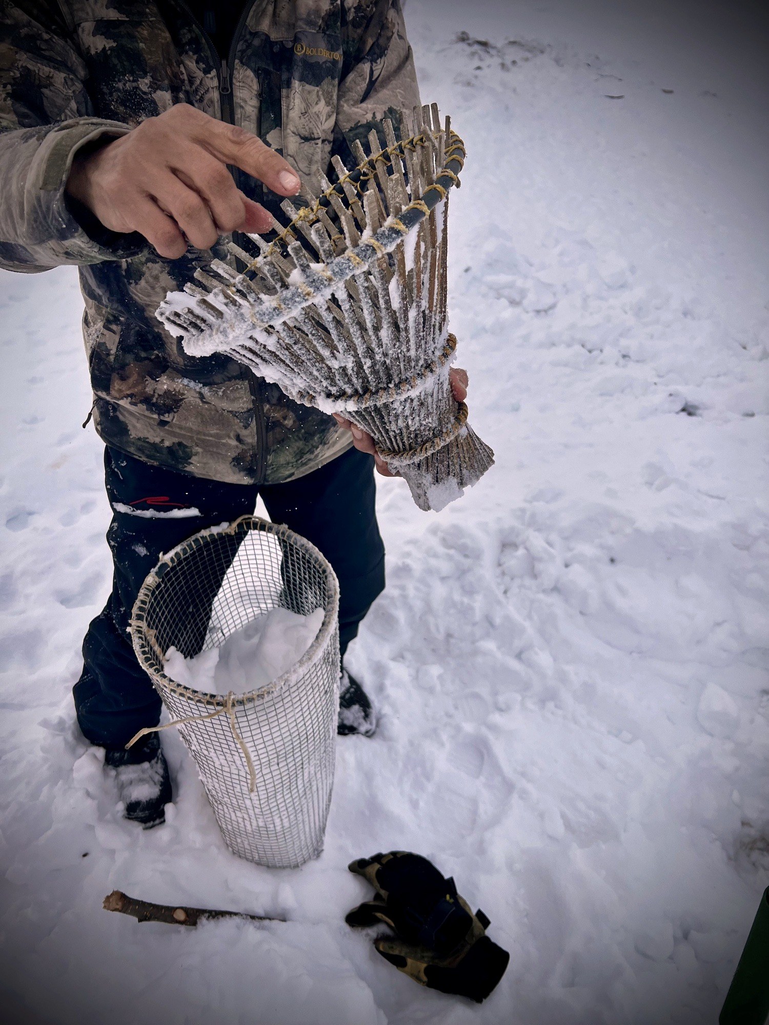 A willow-stick fish trap held over a mesh bait basket on the ice outside Emmonak