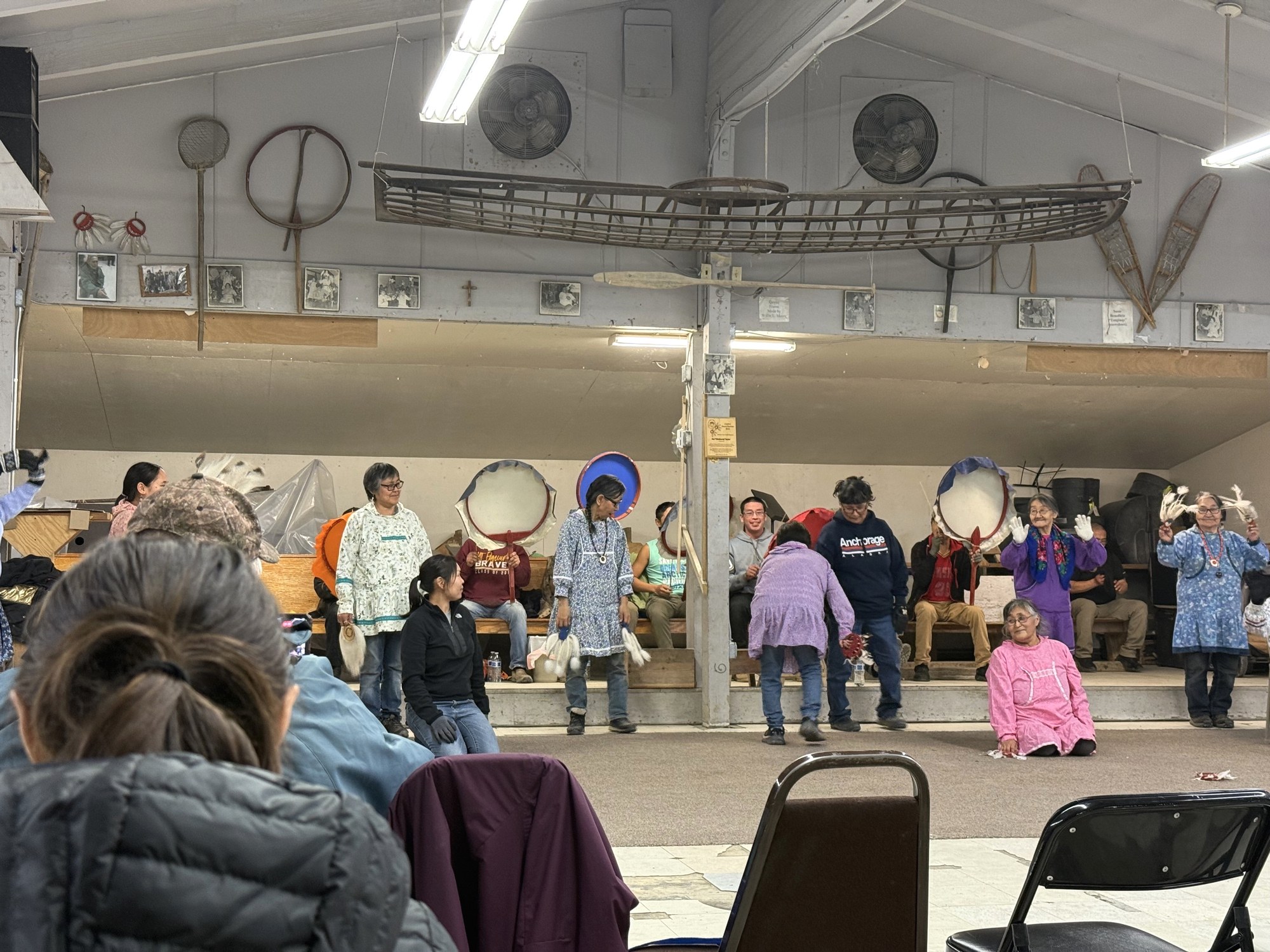 A Yup'ik dance group performing inside an Emmonak community hall, with drums and traditional regalia
